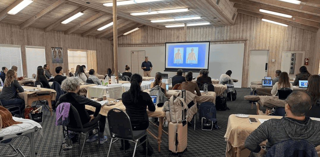 A full classroom of acupuncturists at an AcuSport Education seminar, watching an instructor present an anatomy slide